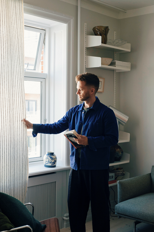 Designer Michael Schneider in his home, in a bright and minimal interior styled with warm materials and designs.